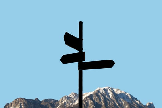 Mountains with black hiking trailhead post showing directions with copy space and blue sky solid background. Concept of travel, hiking and mountaineering. photo