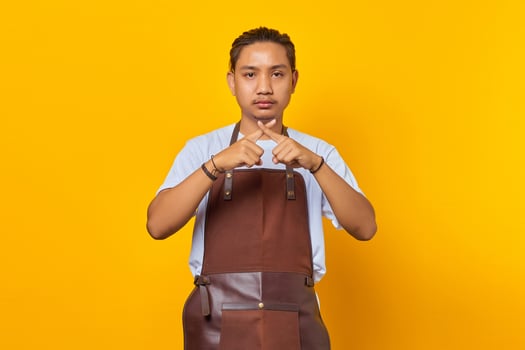 Serious asian young man showing refusal gesture with crossed fingers isolated on yellow background photo