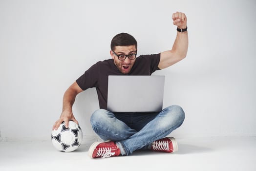 Excited soccer fan with a football isolated on white background. He sits on the floor and watches the results of the game and the best moments of the match on the laptop. photo