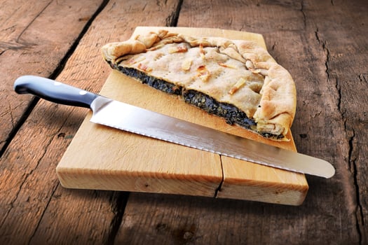 Whole savory pie with bacon cut in half on wooden cutting board photo