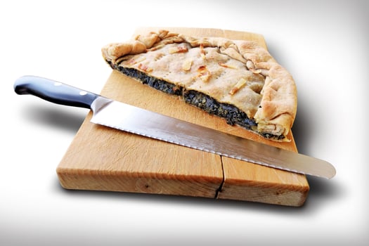 Whole savory pie with bacon cut in half on wooden cutting board photo