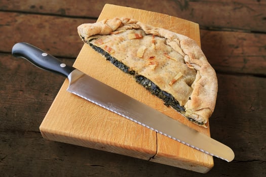 Whole savory pie with bacon cut in half on wooden cutting board photo