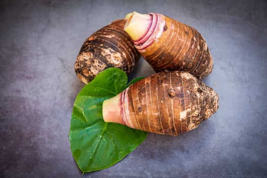 Taro root on taro leaf and dark background, Fresh raw organic taro root ready to cook photo
