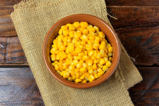 Raw corn kernels inside ceramic bowl on rustic wooden table. space for text photo