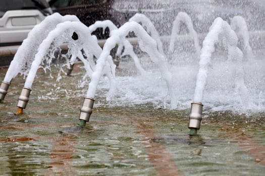 Foamy dense jets of water are frozen in their motion and burst out of the metal nozzles of the city fountain. photo