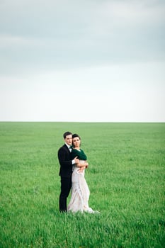 the groom in a brown suit and the bride in an ivory-colored dress on a green field photo