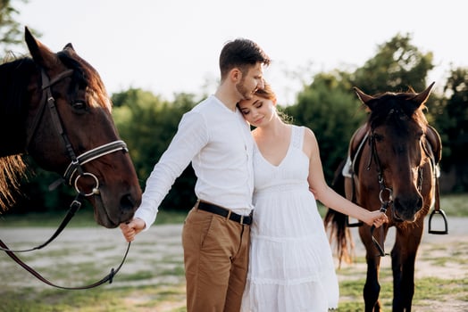 girl in a white sundress and a guy in a white shirt on a walk with brown horses photo