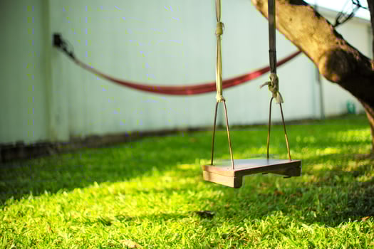 Closeup old wooden swing hanging from the tree in the backyard garden with blurred hammock in background photo