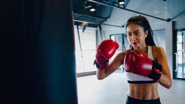 Young Asia lady kickboxing exercise workout punching bag tough female fighter practice boxing in gym fitness class. Sportswoman recreational activity, functional training, healthy lifestyle concept. photo