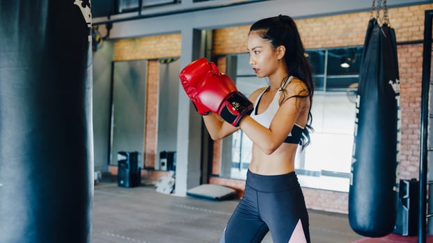 Young Asia lady kickboxing exercise workout punching bag tough female fighter practice boxing in gym fitness class. Sportswoman recreational activity, functional training, healthy lifestyle concept. photo