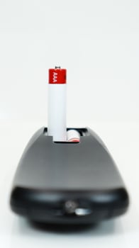 Black TV remote control with AAA alkaline batteries on a white background. Battery replacement, spare parts. Close up of the battery compartment of the remote control. Vertical photography. photo