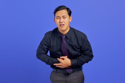 Photo of handsome businessman suffering from painful stomach ache on purple background