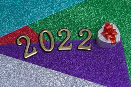 On a colorful bright shiny New Year background, a silver gift box with a red bow and golden numbers 2022. Concept for New Year's card photo
