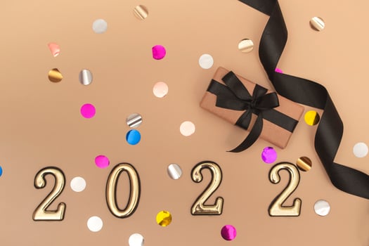 View from above. Beige background with star confetti, gift box with black ribbon and golden numbers. Happy new year 2022 greeting card. photo