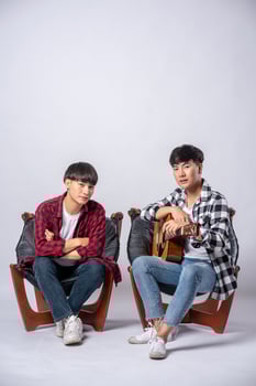 Two young men sitting in a chair holding a guitar photo
