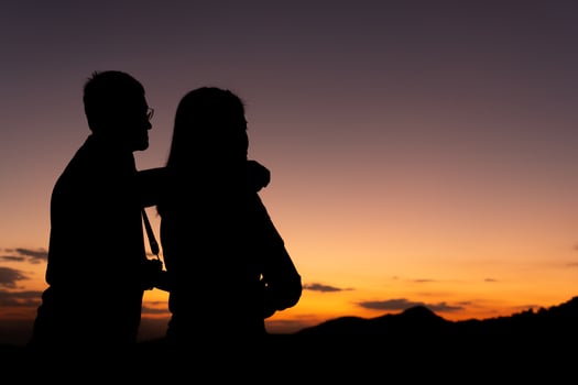 silouette of man and woman as a couple looking at sunset behind the moutain photo