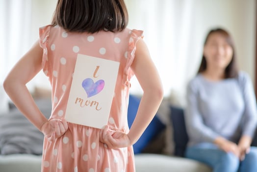 Asian cute girl hide handmade greeting card with i love mom word to give surprising her mother at home photo