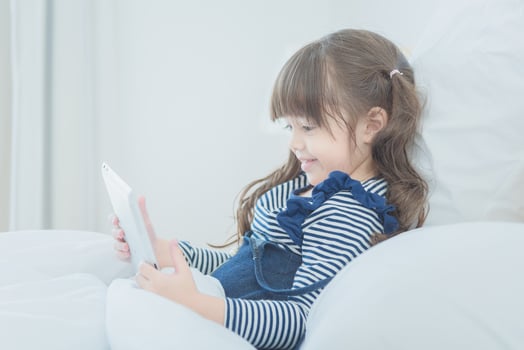 Cute little girl enjoy watching cartoon on smart tablet with cute doll while sitting on bed in kid's bedroom at home photo