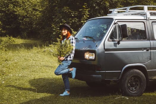 Woman in hat holding fern leaves standing near the van on background of green grass photo