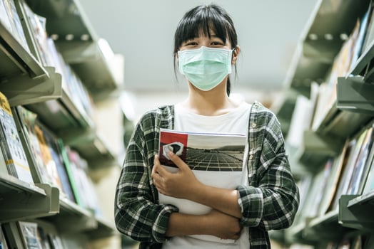 A woman wearing a mask and searching for books in the library. photo