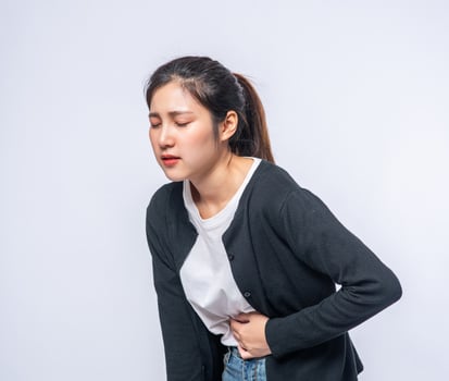 A woman standing with a stomach ache and presses her hand on her stomach. photo