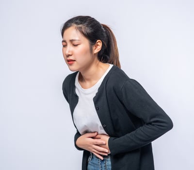 A woman standing with a stomach ache and presses her hand on her stomach. photo