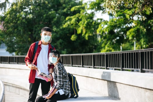 Male and female students wearing masks sit and read books on the stairs photo