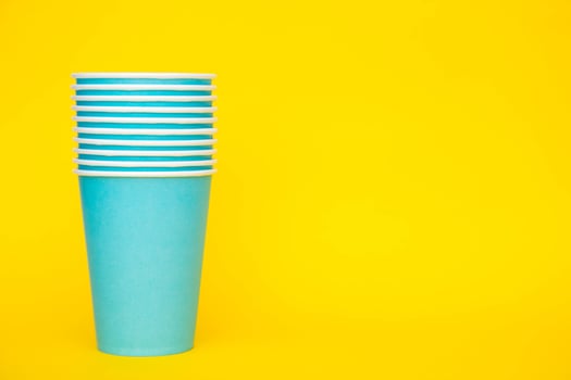 Many blue paper disposable cups on yellow background. Set for party photo