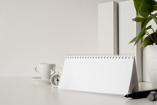 Mock up blank spiral calendar with flipping sheets on white table with coffee, stationery and clock photo