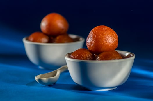 Indian Dessert Gulab Jamun in bowl with spoon on blue background photo