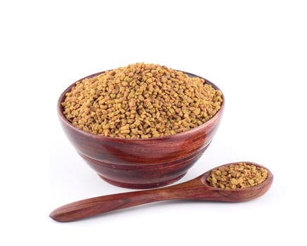 Fenugreek seeds in wooden bowl with spoon isolated on white background photo