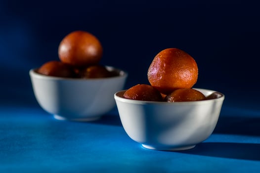 Indian Dessert Gulab Jamun in bowl with spoon on blue background photo