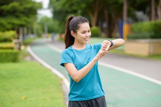 Happy young woman in sportswear using smart watch while exercising in park photo