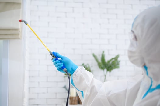 A medical staff in PPE suit is using disinfectant spray in living room, Covid-19 protection , disinfection concept . photo