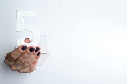 Female hand holding up the number 5 against a white photo