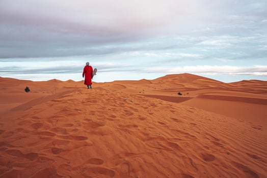 Man in traditional clothes with sandboard standing on sand dunes against sky photo