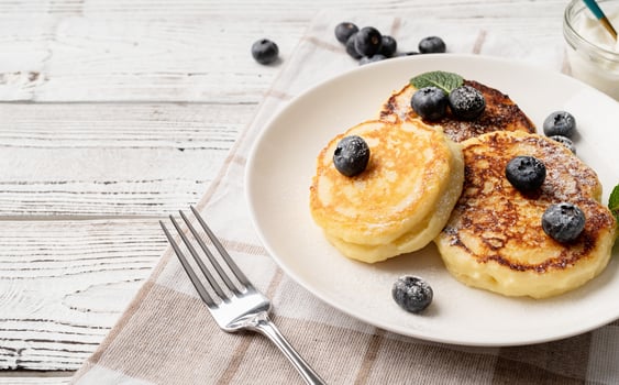 Cottage cheese pancakes served with curd and blueberries, high angle view on wooden background, copy space photo