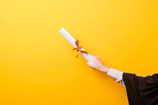 Close up of woman hand in graduation gown is holding graduation cap and certificate on yellow background photo
