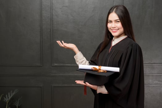 Portrait of young woman in graduation gown smiling and cheering on black background photo