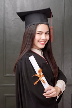 Portrait of young woman in graduation gown smiling and cheering on black background photo