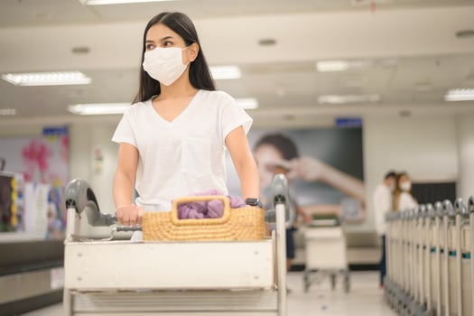 A traveling woman wearing protective mask in the airport with luggage on trolley, travel under Covid-19 pandemic, safety travels, social distancing protocol, New normal travel concept photo