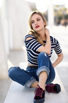 Blonde woman, model of fashion, sitting in urban background. photo