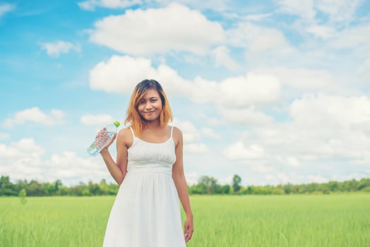 Women lifestyle concept young pretty  woman wearing white dress holding bottle of water at grassland smiley to camera look so fresh enjoy and happy. photo