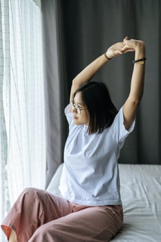 A woman in a white shirt sitting on the bed and raising both arms. photo