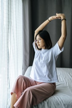 A woman in a white shirt sitting on the bed and raising both arms. photo