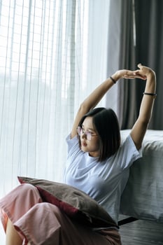 A woman in a white shirt sitting on the bed and raising both arms. photo