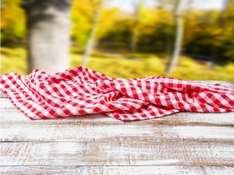 checkered tablecloth on old wooden table on blurred park background, holiday concept photo