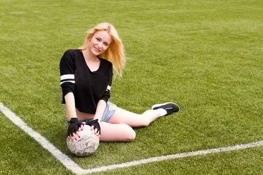 The girl is sitting on the football field with the ball. photo