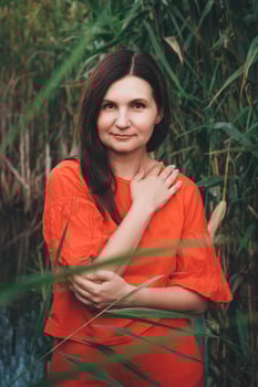 Woman dressed in red clothes standing against backdrop of reeds and lake photo