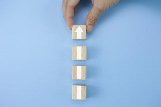 Closeup man hand arranging wood cube stacking as step stair with arrow up symbol photo